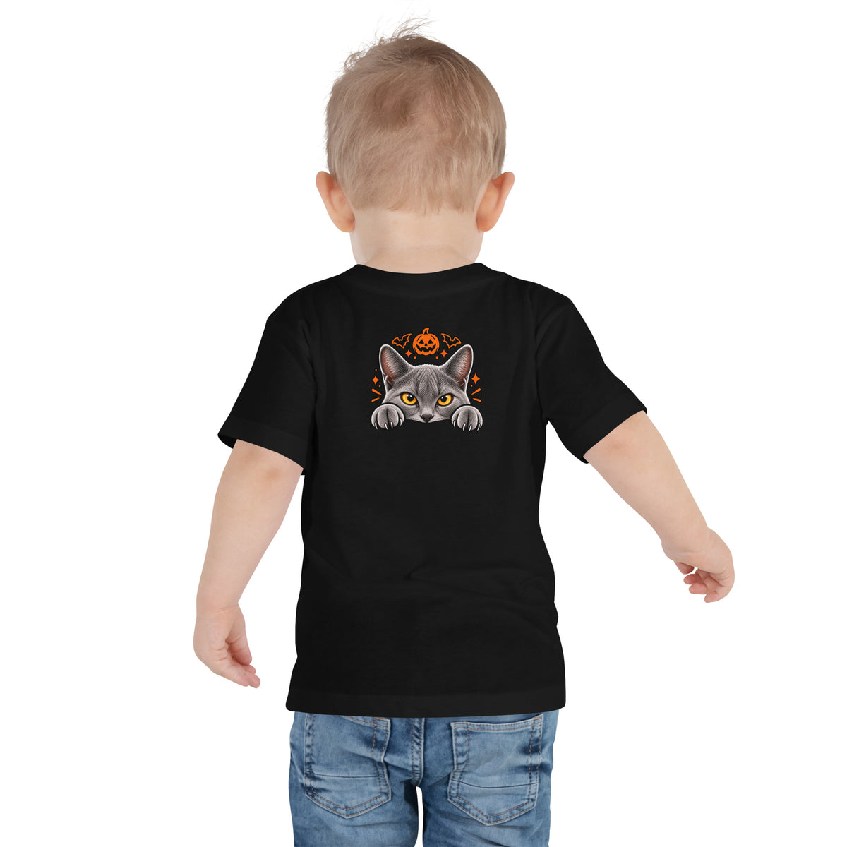 Back view of a toddler wearing a black Halloween tee with Uno the gray cat peeking over an edge, framed by an orange pumpkin and festive spooky accents.
