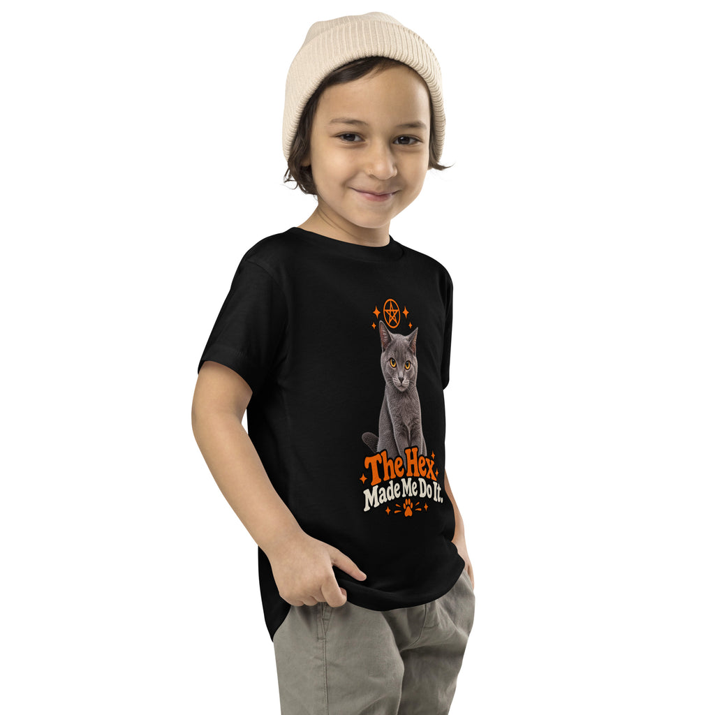 Angled view of a child wearing the black Uno the Cat toddler tee, showing the orange-and-cream “The Hex Made Me Do It” Halloween graphic.